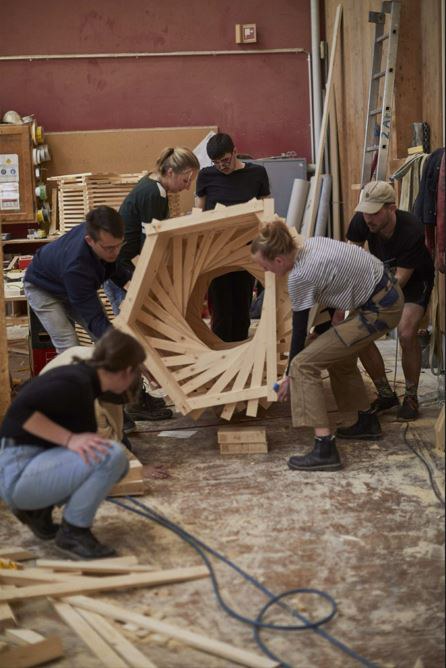 Architekturstudierende bauen gemeinsam in einer Werkstatt einen Turm aus Holz