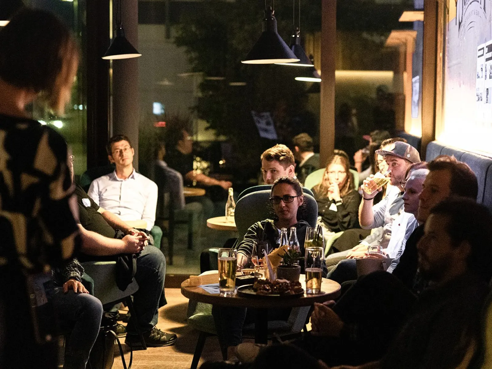 Alumni-Treffen in gemütlicher Atmosphäre: Eine Gruppe von Menschen sitzt in einer Lounge, unterhält sich und genießt Getränke.