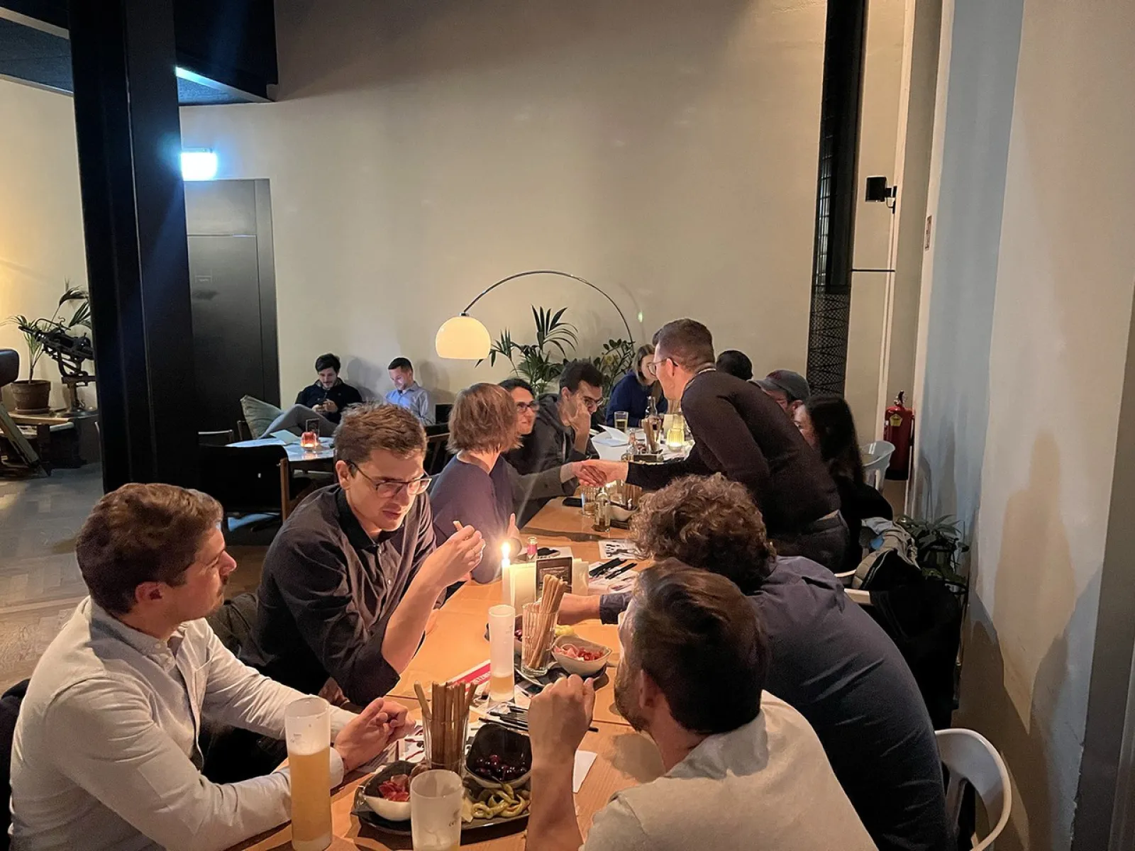 Alumni-Treffen in einem gemütlichen Restaurant: Mehrere Personen sitzen an einem langen Tisch, unterhalten sich und genießen Speisen und Getränke in entspannter Atmosphäre.