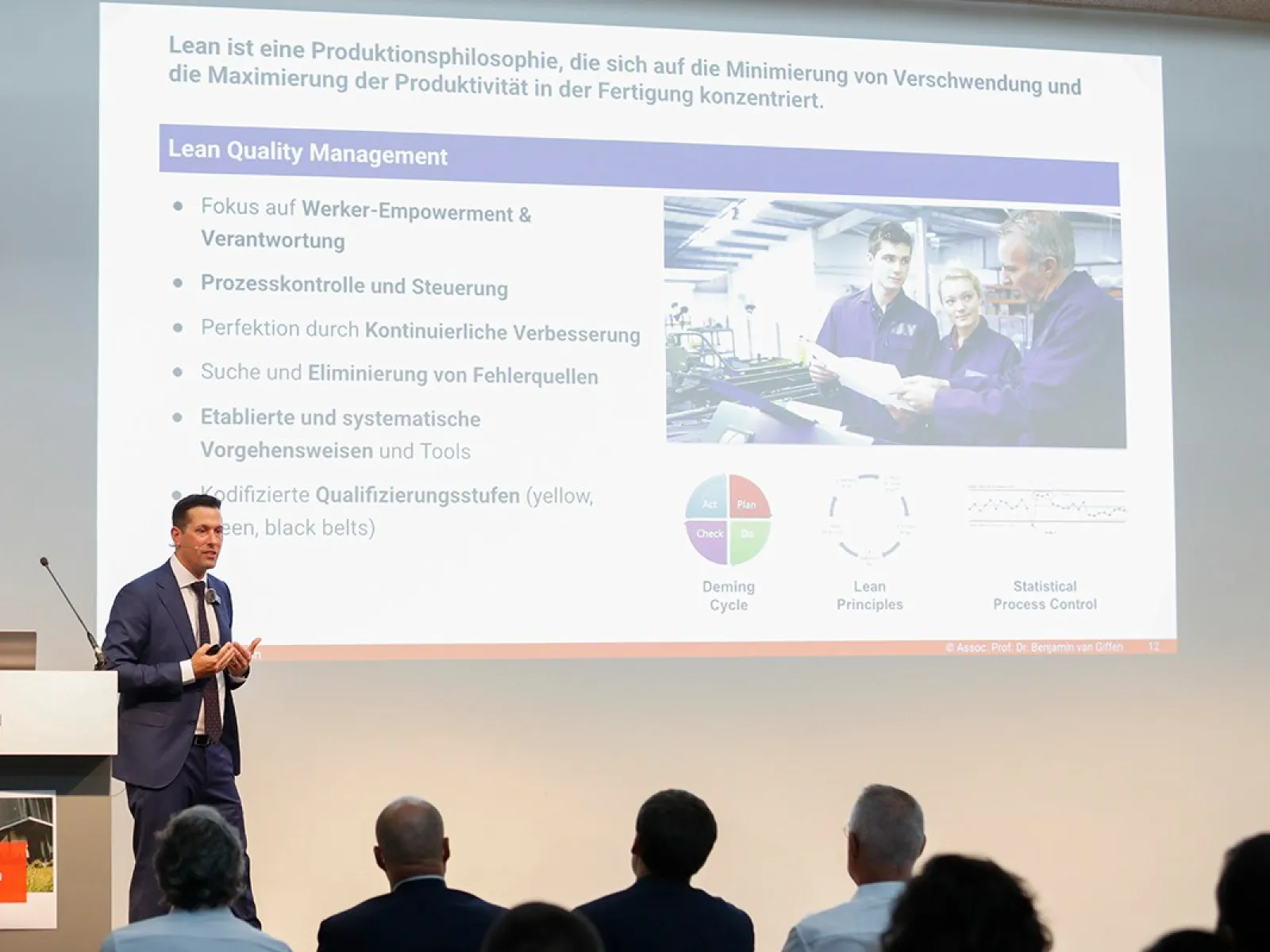 Foto von Assoz. Prof. Dr. Benjamin van Giffen während seiner Antrittsvorlesung an der Universität Liechtenstein mit dem Titel 'Tradition trifft Technologie' vor einem Publikum, darunter Rektor Dr. Christian Frommelt und andere Würdenträger.