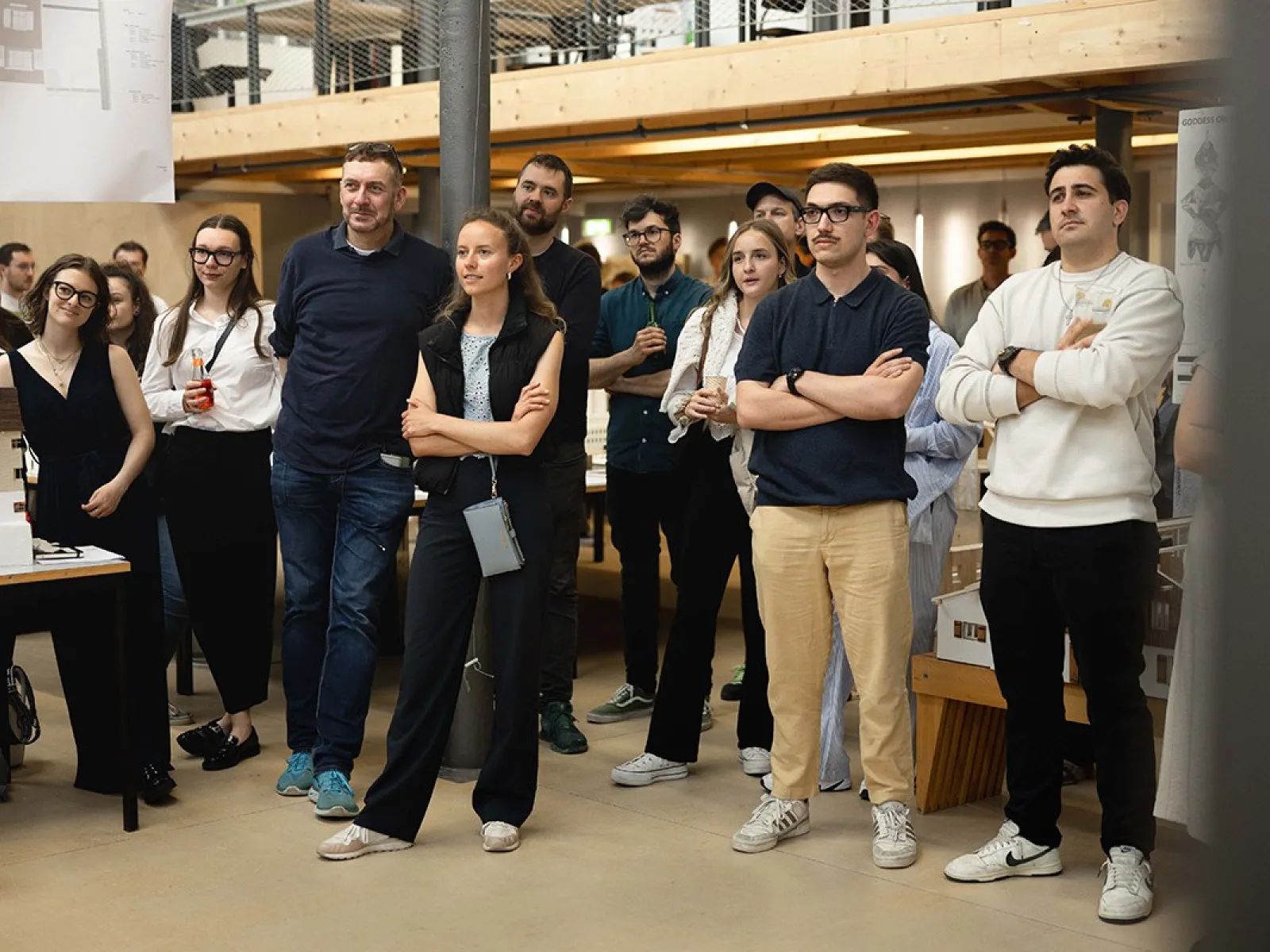 Eine Gruppe von Menschen steht in einem Innenraum der Universität Liechtenstein, aufmerksam einem Ereignis folgend. Im Hintergrund sind architektonische Modelle und eine Galerieebene zu sehen. Die Atmosphäre wirkt interessiert und gespannt.