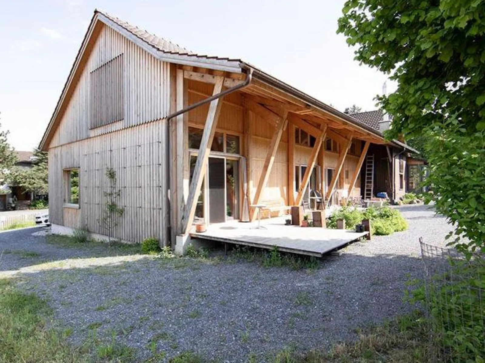 Ein modernes Holzgebäude mit schrägen Stützen und einer Terrasse, umgeben von Kies und Grünflächen, im ländlichen St. Galler Rheintal.