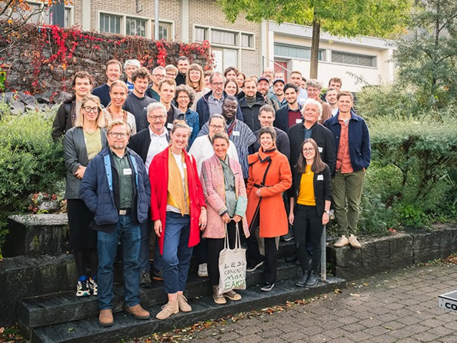 Gruppe von Menschen steht lächelnd auf einer Treppe im Freien, umgeben von grüner Vegetation. Sie tragen Namensschilder und sind für ein Symposium an der Universität Liechtenstein versammelt.
