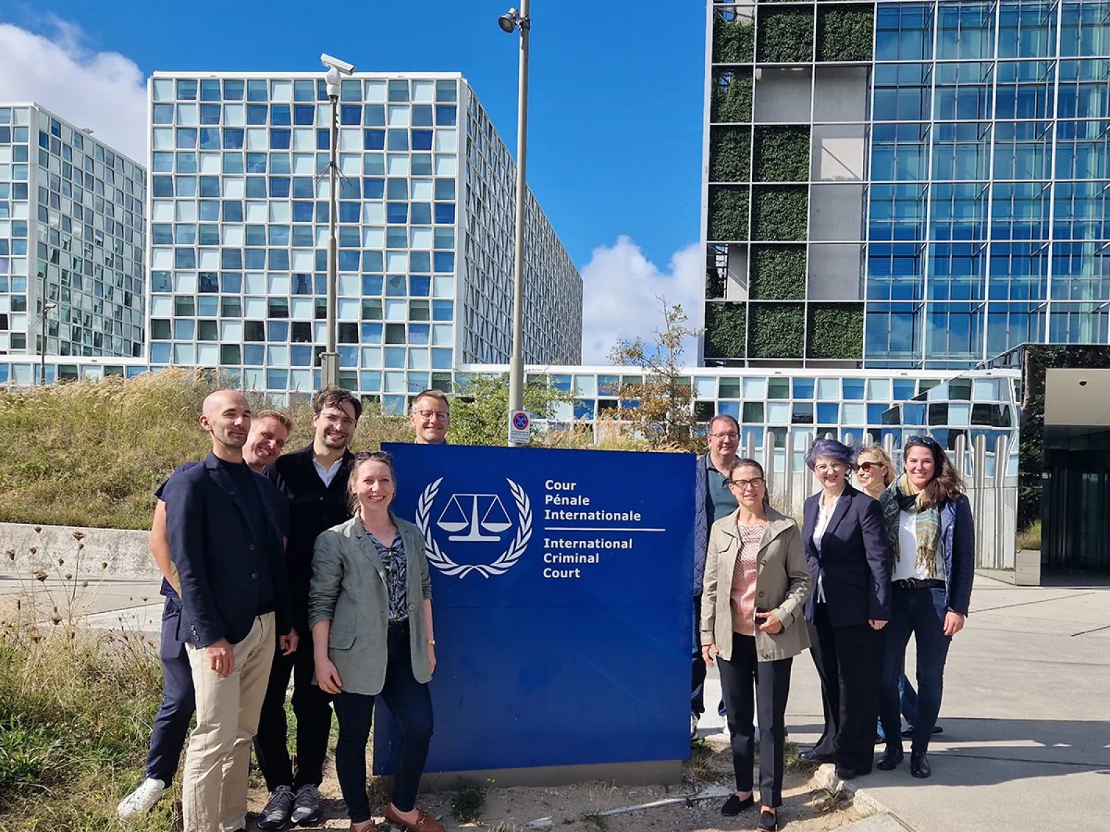 Gruppe von Studierenden des Executive Master of Laws (LL.M.) im Wirtschaftsstrafrecht vor dem Internationalen Strafgerichtshof in Den Haag, lächelnd und posierend vor dem Gebäude mit dem Logo des Gerichtshofs.