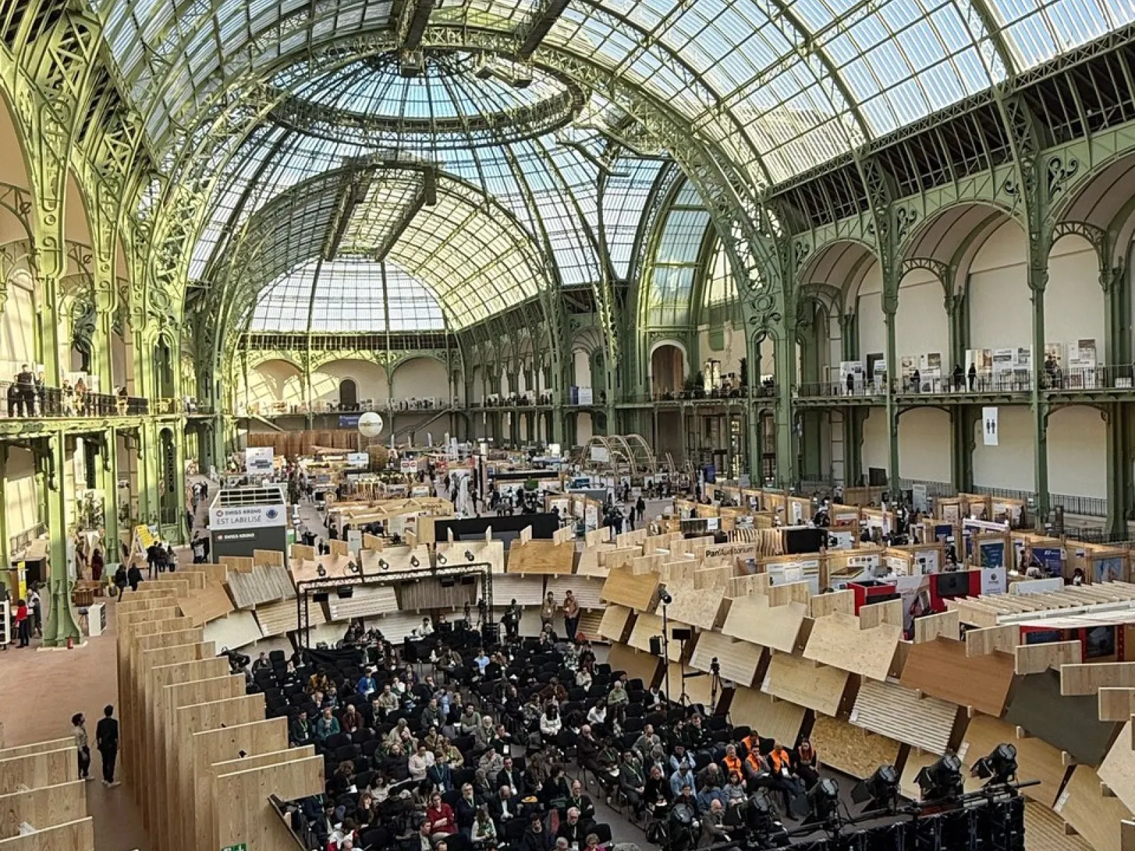 Ein großes, lichtdurchflutetes Konferenzzentrum mit einer beeindruckenden Glas- und Stahlarchitektur. Zahlreiche Teilnehmer sitzen in einem Auditorium, umgeben von Holzstrukturen, die innovative Bauweisen präsentieren.
