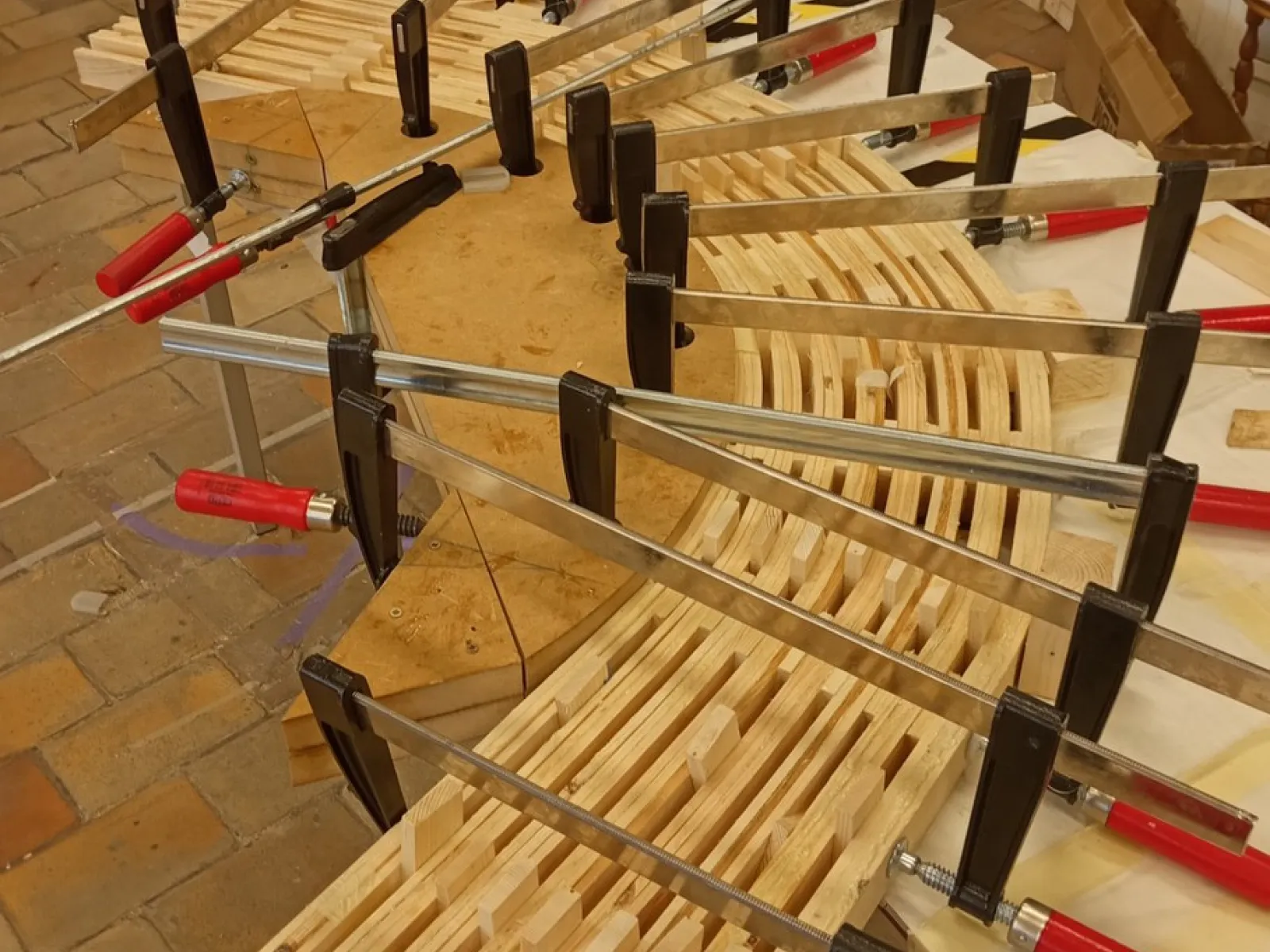 Ein Holzmodell eines Möbelstücks wird mit mehreren Schraubzwingen auf einem Tisch fixiert. Das Bild zeigt den handwerklichen Prozess der Studierenden während der «Maak Week» an der Universität Antwerpen.