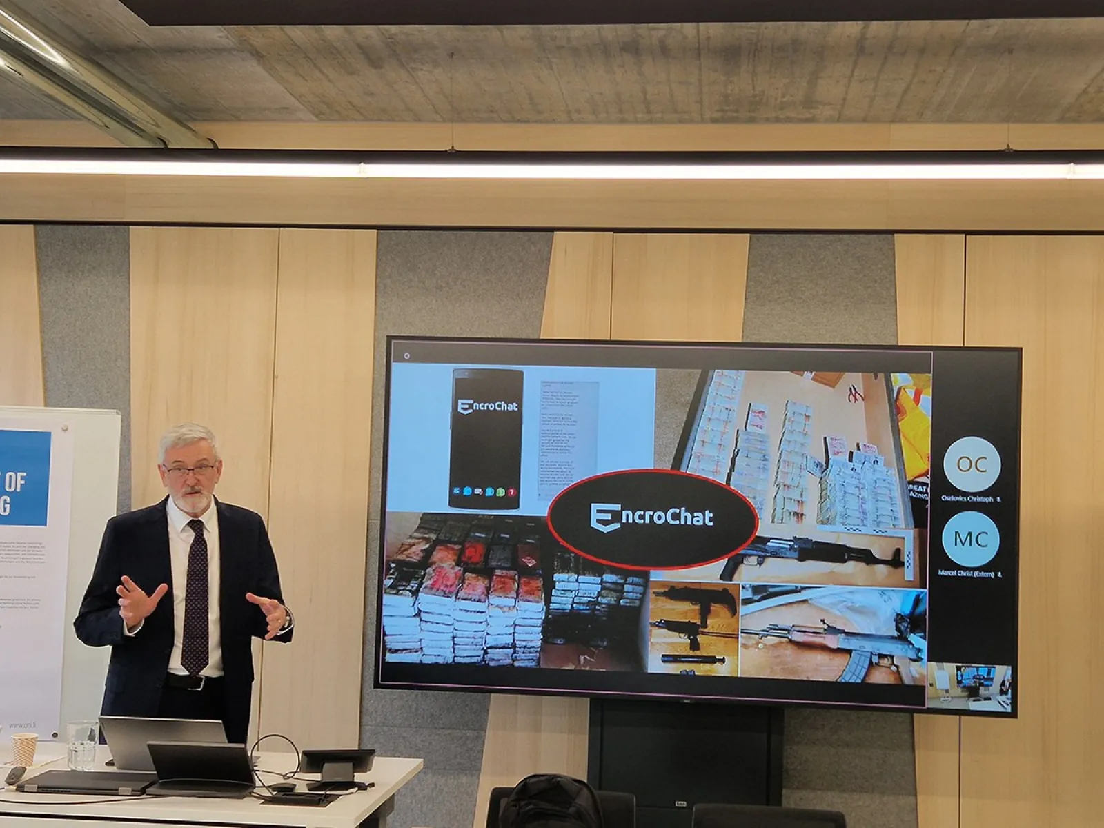 Ein Vortragender steht vor einem Bildschirm, der eine Präsentation über EncroChat zeigt. Der Raum wirkt modern und ist für eine akademische Veranstaltung eingerichtet.