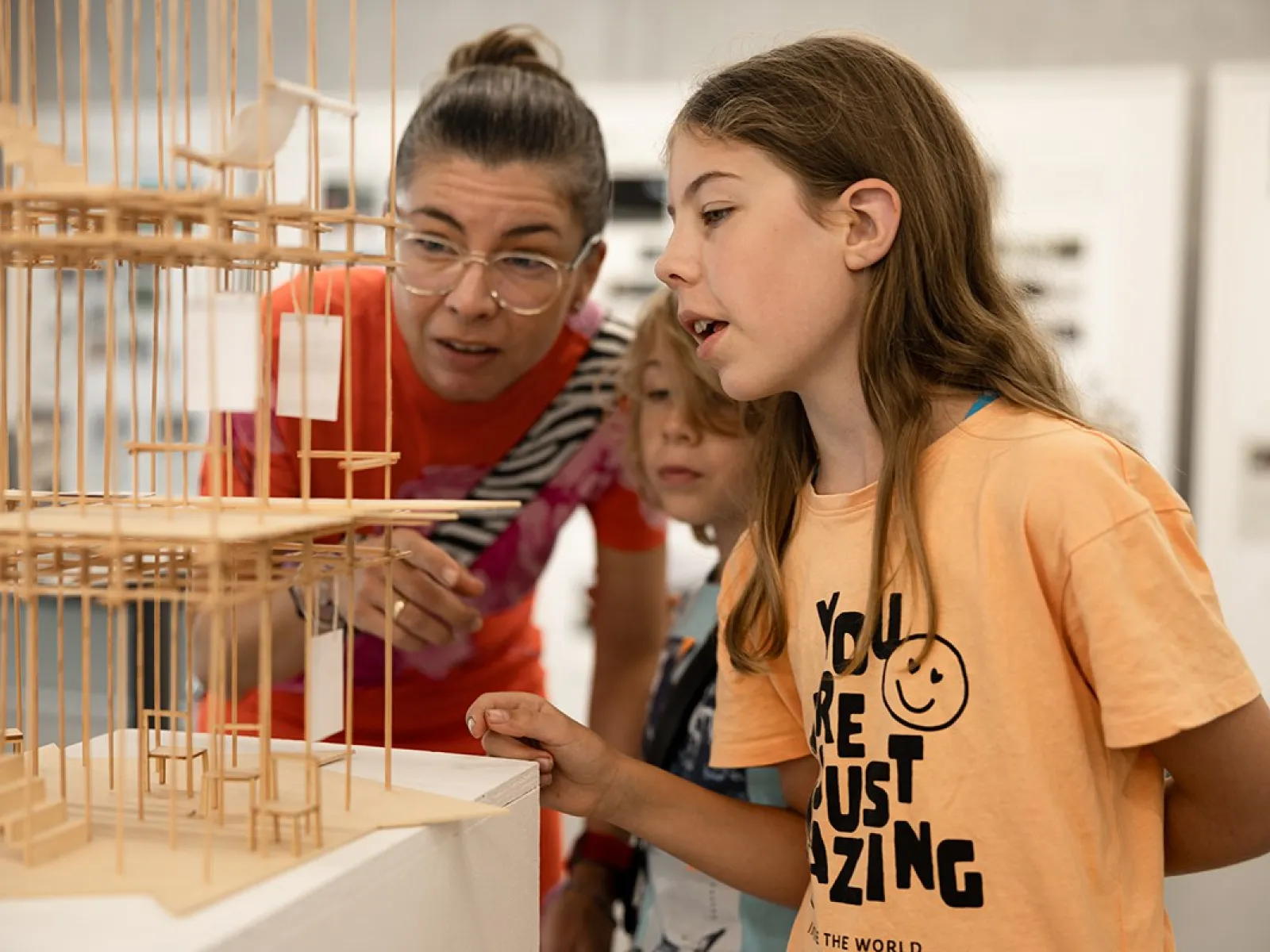 Eine Frau und zwei Kinder betrachten ein detailliertes Architekturmodell aus Holz. Die Szene findet in einem Ausstellungsraum statt, der Teil des Tags der offenen Tür an der Universität Liechtenstein ist.