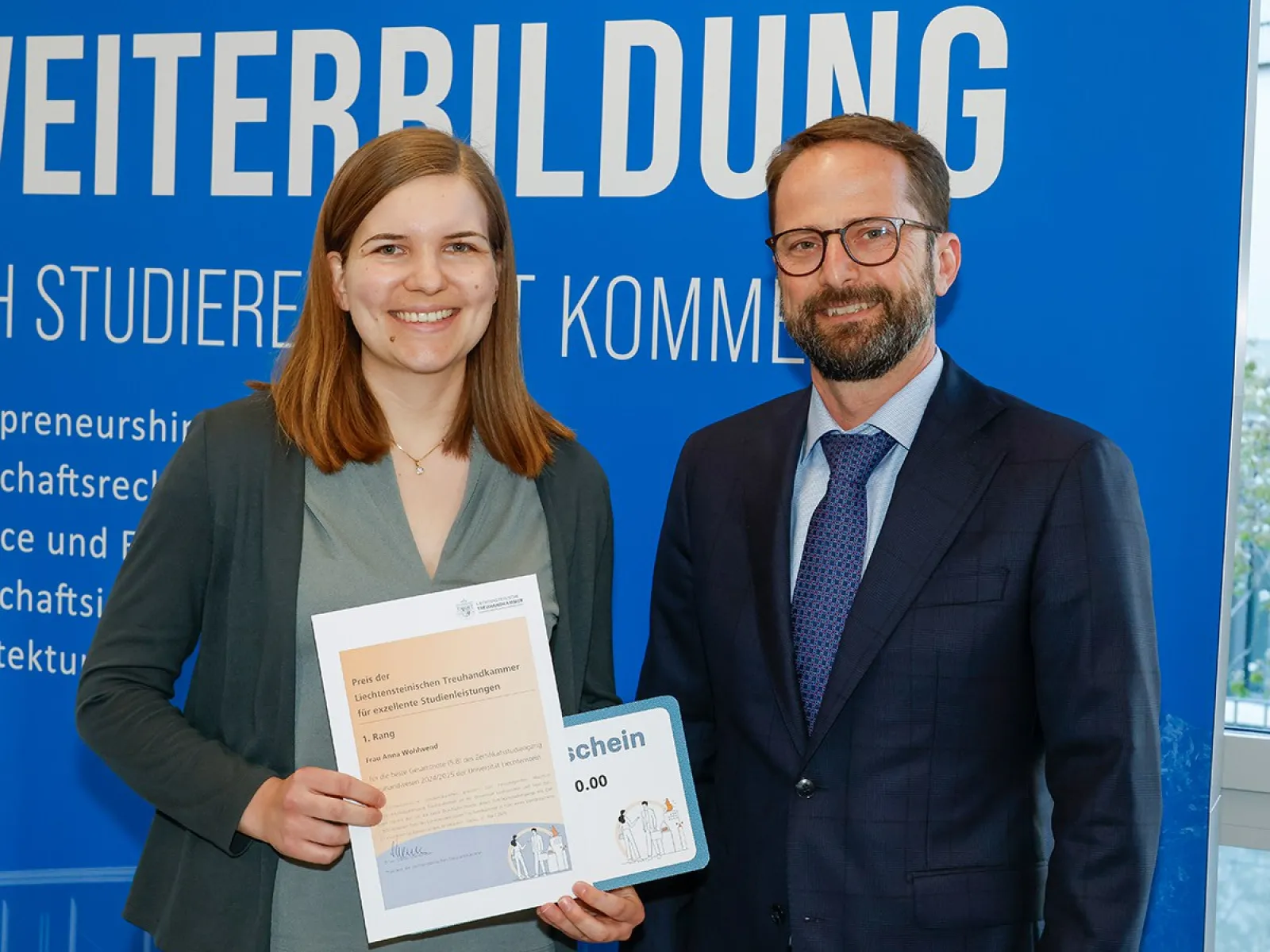 Eine Absolventin des Zertifikatsstudiengangs Treuhandwesen an der Universität Liechtenstein erhält eine Auszeichnung. Sie steht neben einem Mann vor einem blauen Hintergrund mit dem Schriftzug "Weiterbildung".