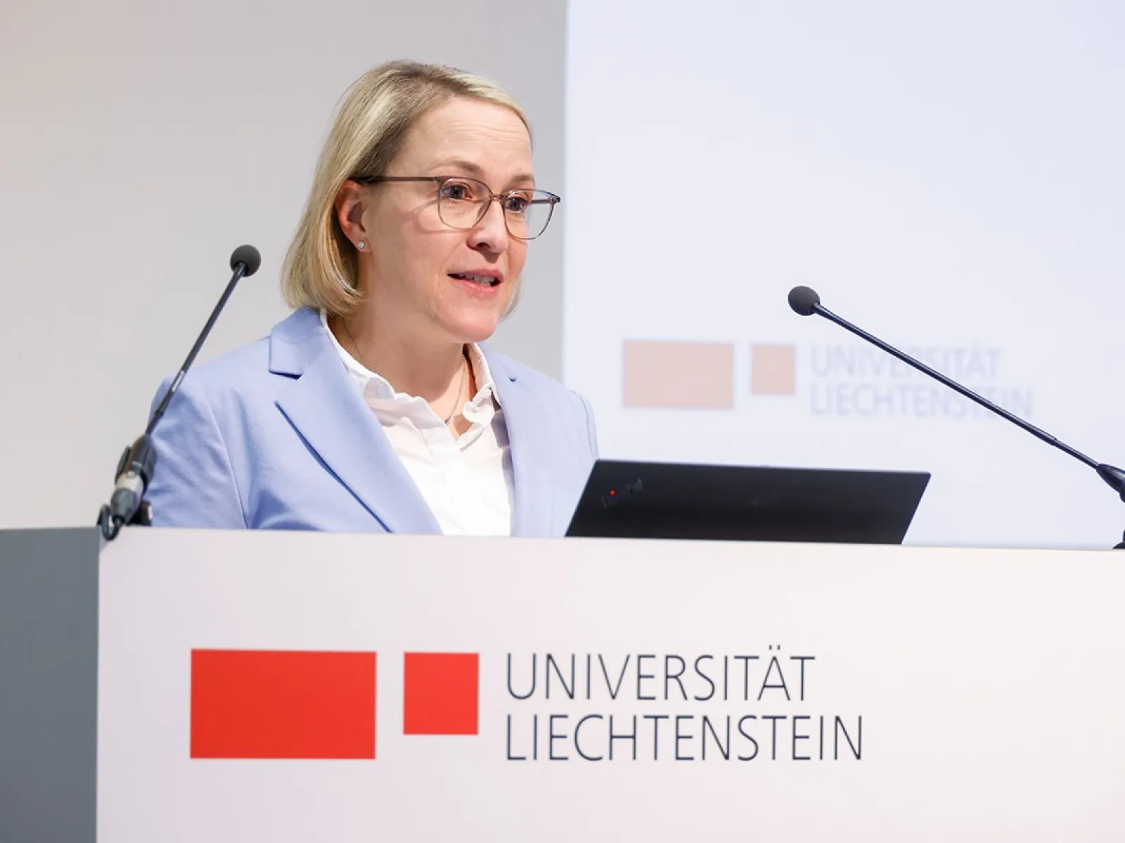 Eine Person hält eine Rede am Rednerpult der Universität Liechtenstein. Im Hintergrund ist das Logo der Universität zu sehen.