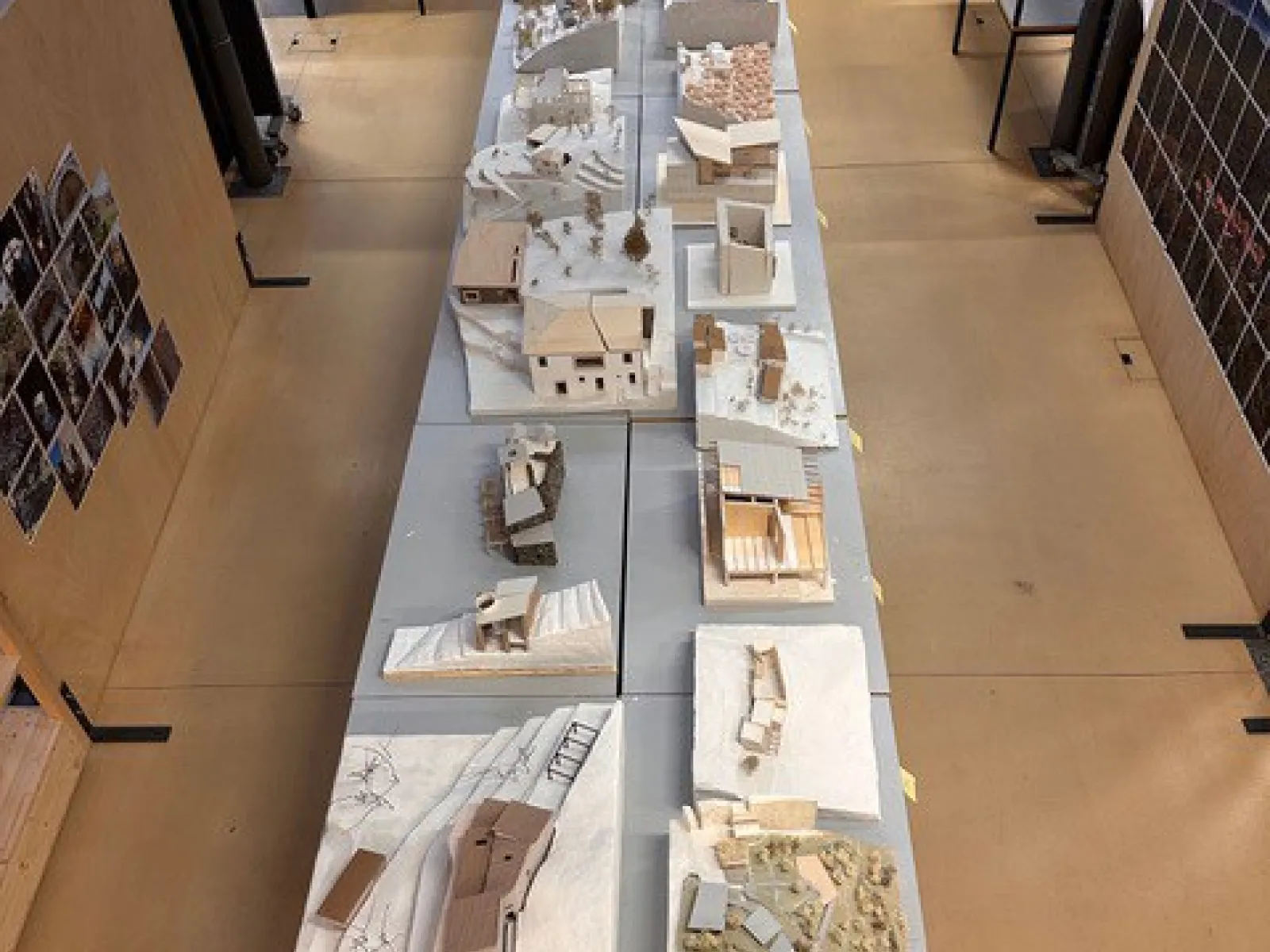 Eine Reihe von Architekturmodellen auf Tischen in einem Studio. Die Modelle zeigen verschiedene Gebäude und Landschaften, die im Rahmen eines Projekts des Advanced Studios Upcycling der Universität Liechtenstein erstellt wurden. Im Hintergrund sind Regale und weitere Arbeitsbereiche zu sehen.