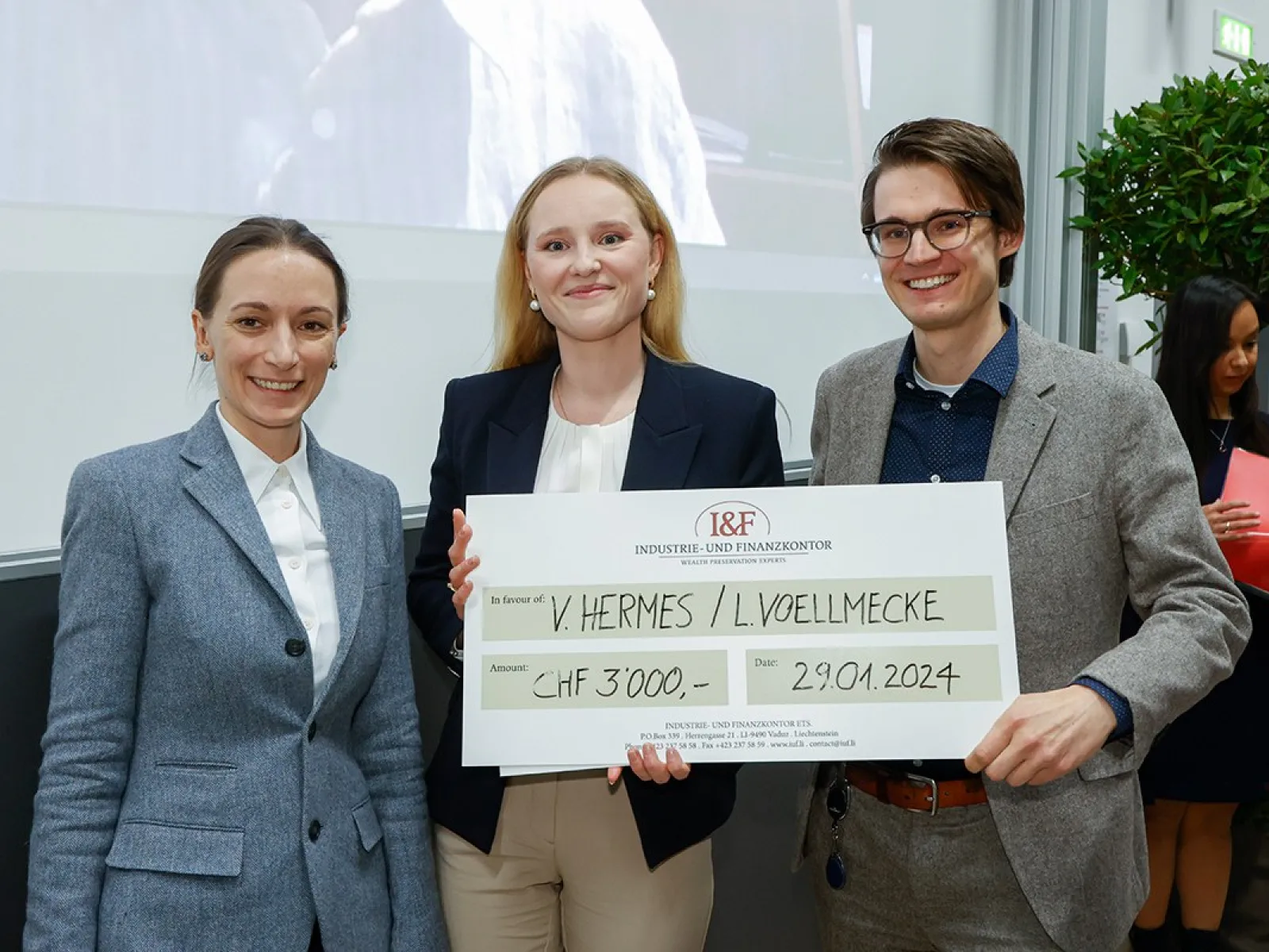 Drei Personen halten einen großen Scheck mit der Aufschrift "I&F Family Wealth Preservation Award" in einem Veranstaltungsraum. Sie lächeln in die Kamera.