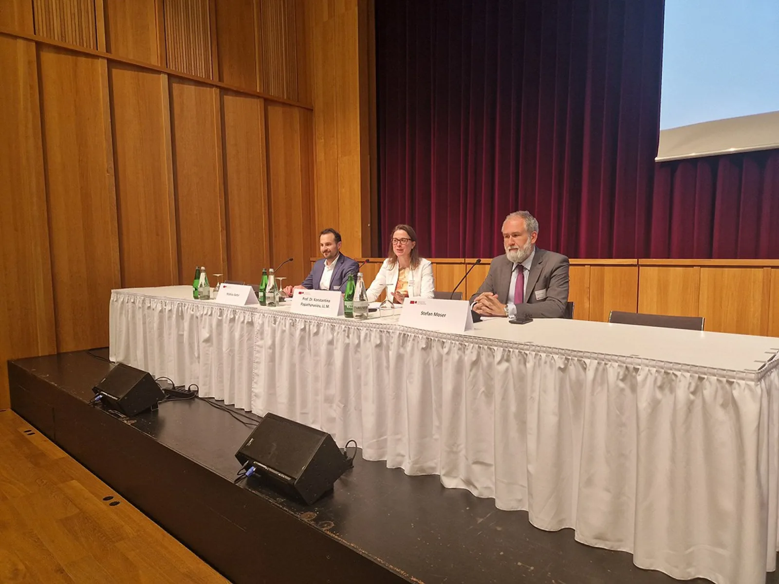 Podiumsdiskussion beim Compliance-Day 2024 an der Universität Liechtenstein. Drei Personen sitzen hinter einem Tisch mit Mikrofonen und Getränken. Der Raum hat Holzwände und einen roten Vorhang im Hintergrund.