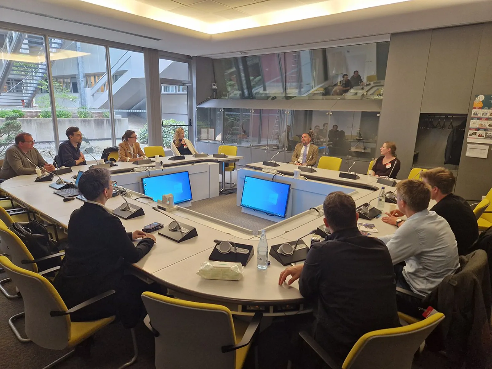 Studierende des Executive Master of Laws (LL.M.) im Wirtschaftsstrafrecht sitzen in einem modernen Konferenzraum des Europarats in Straßburg. Sie nehmen an einer Diskussion teil, geleitet von einem Vortragenden. Laptops und Notizen sind auf dem Tisch verteilt.