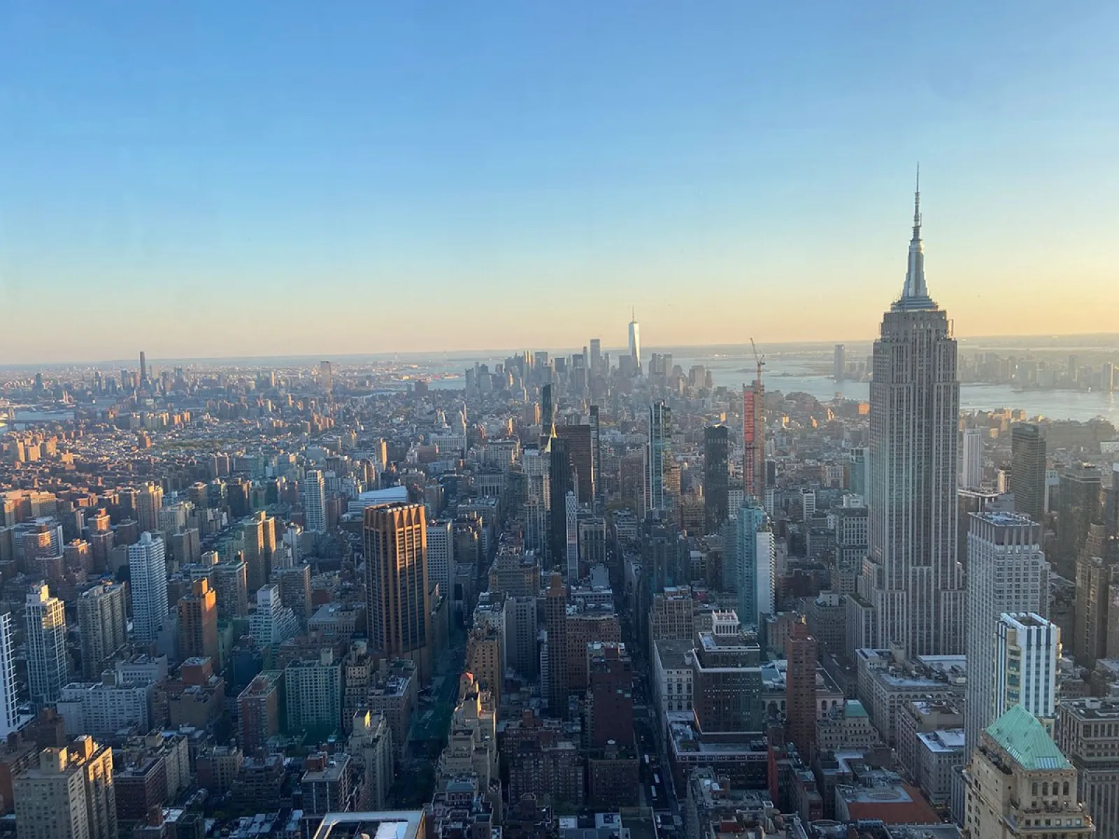 Luftaufnahme von New York City bei Sonnenuntergang, mit dem Empire State Building im Vordergrund und der Skyline im Hintergrund.