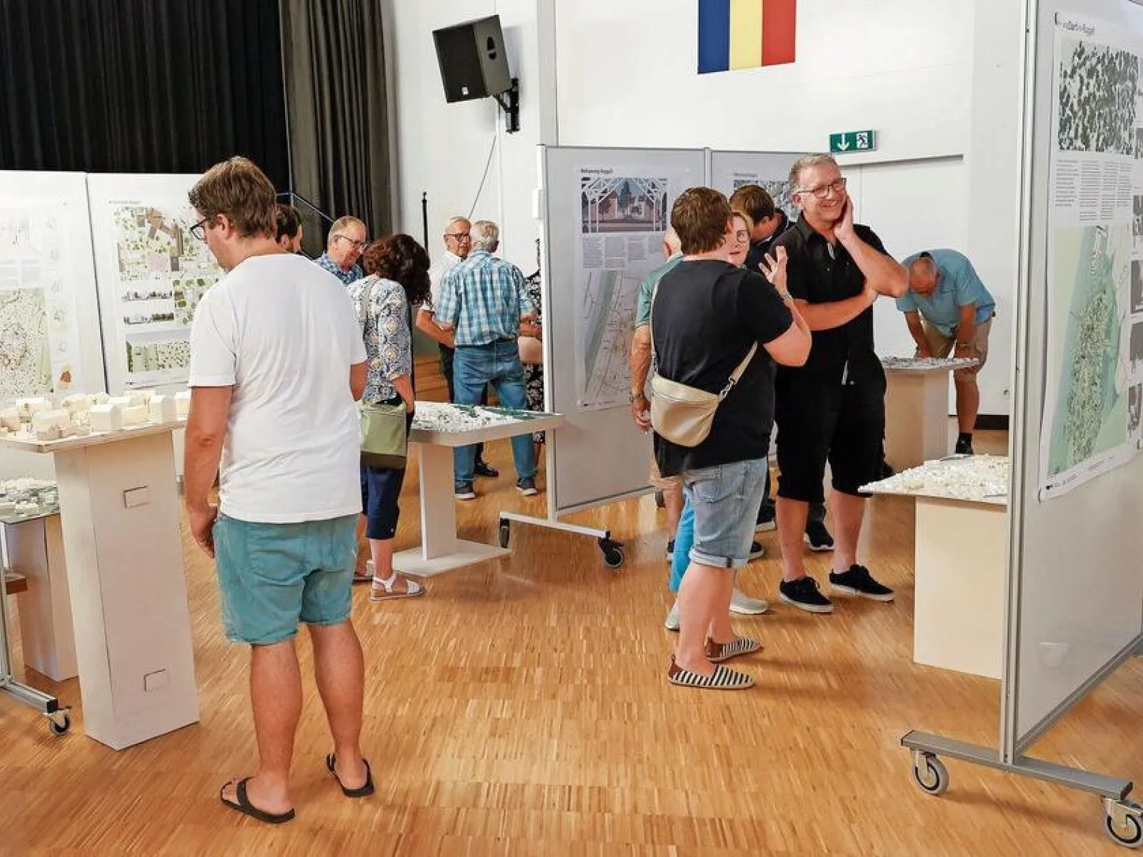 Menschen betrachten Architekturmodelle und Plakate in einer Ausstellungshalle. Die Veranstaltung zeigt studentische Projekte zur Ortsentwicklung in Ruggell, präsentiert von der Universität Liechtenstein.