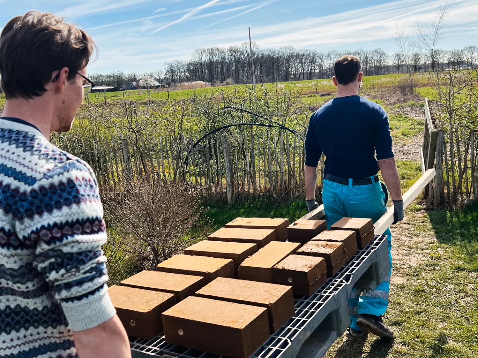 Lehmziegel, die von zwei Männern zu einer Baustelle transportiert werden