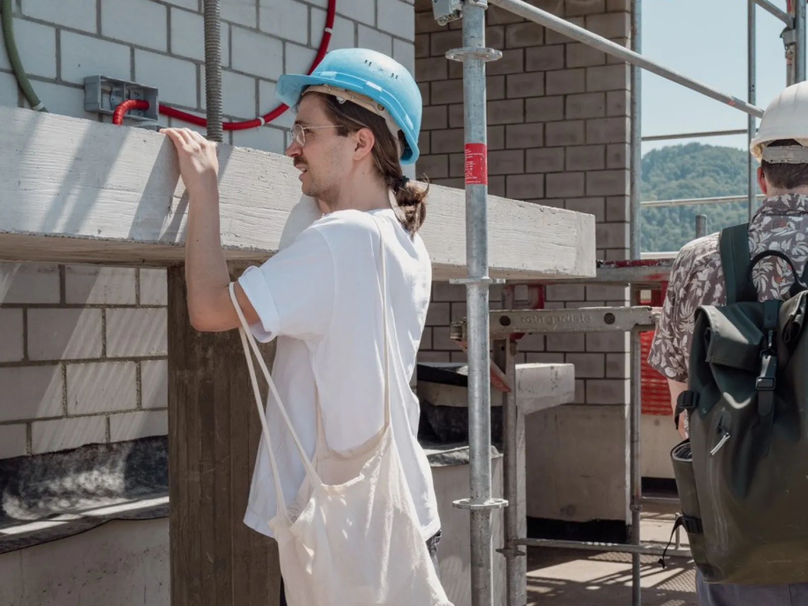 Ein Mann mit einem Bauhelm und einer Baumwolltasche inspiziert eine Baustelle 