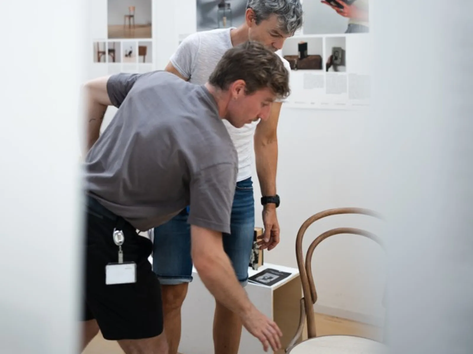 Zwei Männer bücken sich zu einem Kaffeehausstuhl in einer Ausstellung