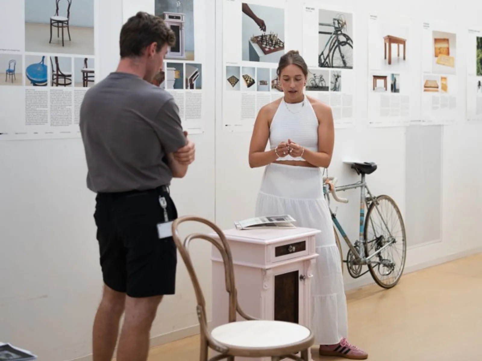Ein Mann und eine Frau stehen in einer Ausstellung mit einem Kaffeehausstuhl im Vordergrund 