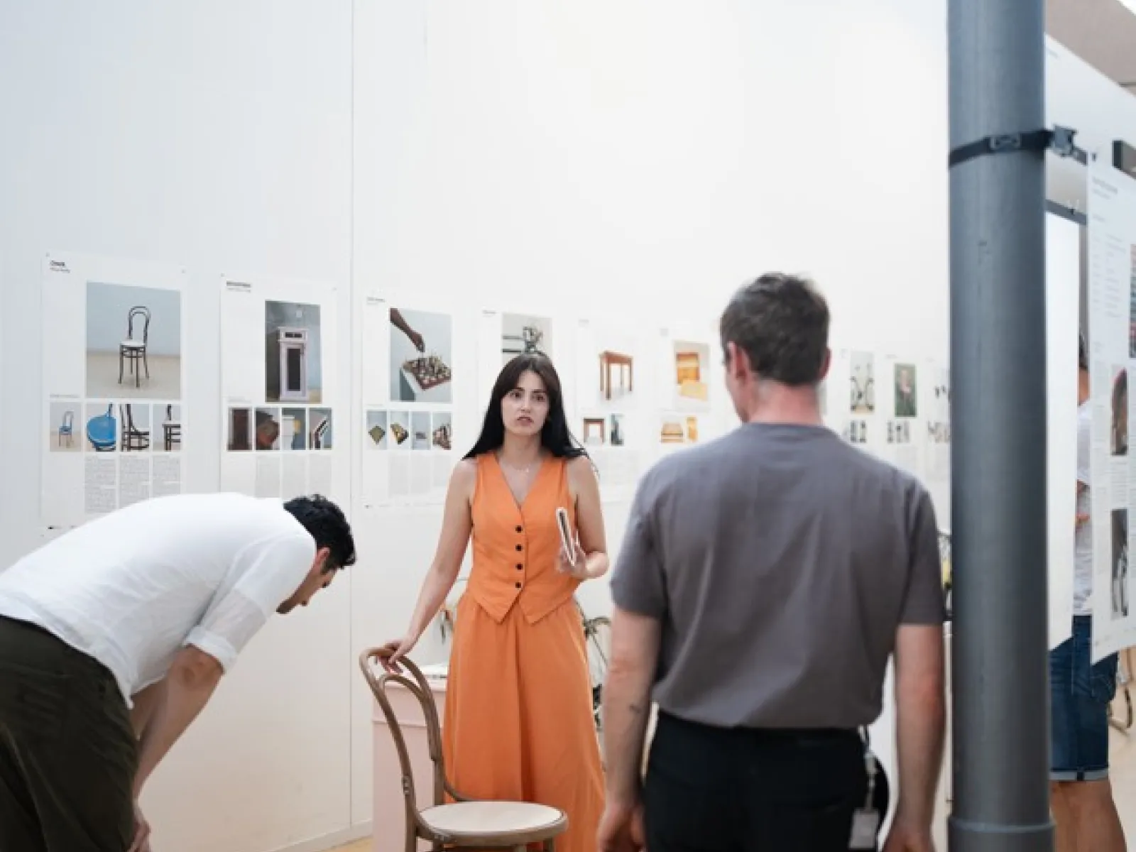 Zwei Männer und eine Frau mit oranger Kleidung stehen in einer Ausstellung 