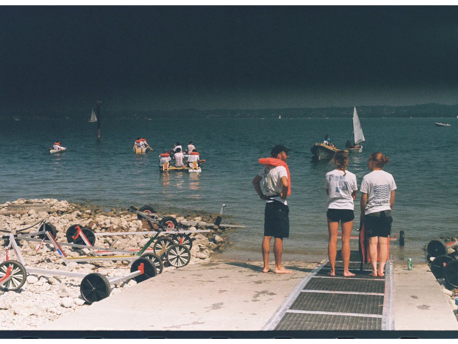 Mehrere Menschen stehen vor einem See und schauen auf Boote. 