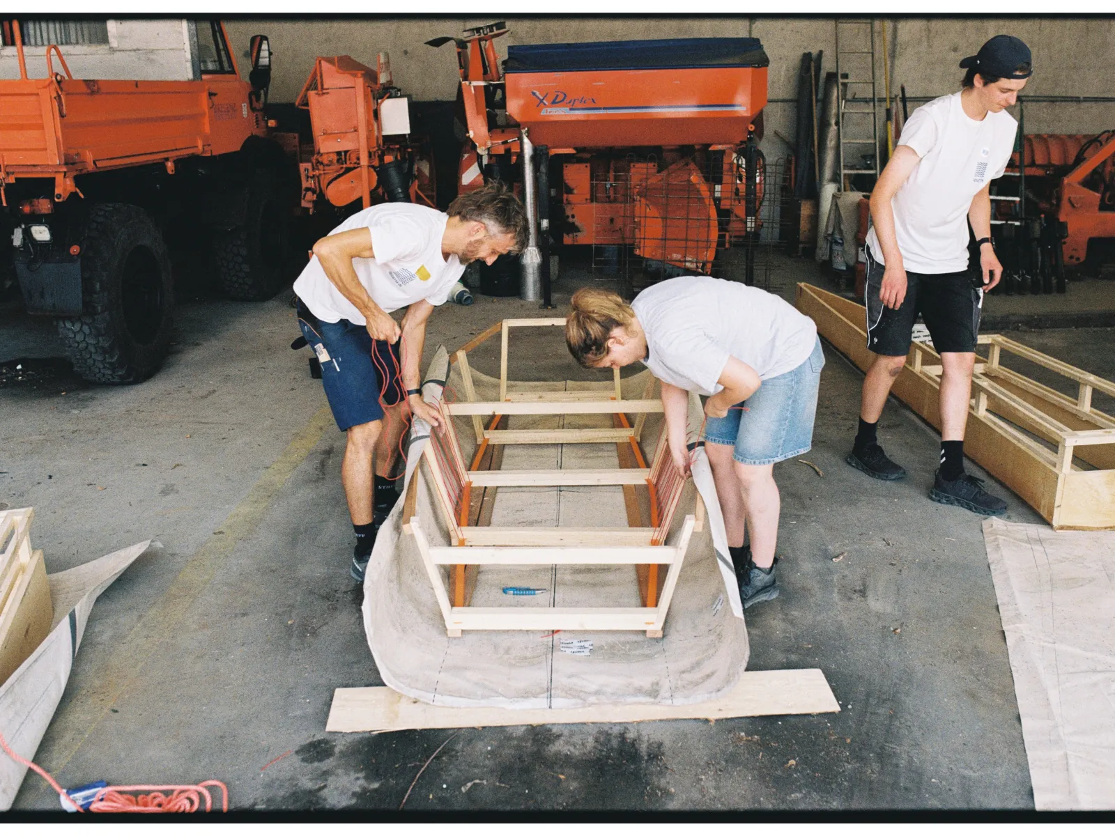 Drei Personen in einer Werkstatt, die an einem Boot arbeiten. 