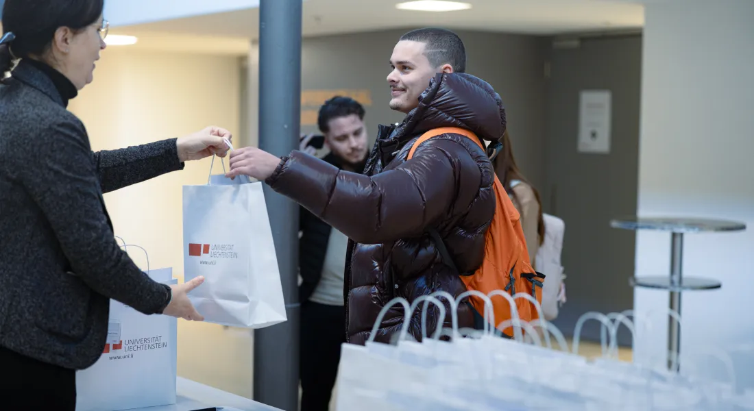 Ein Student erhält bei der Anmeldung an der Universität Liechtenstein eine Willkommens-Tasche mit dem Uni-Logo