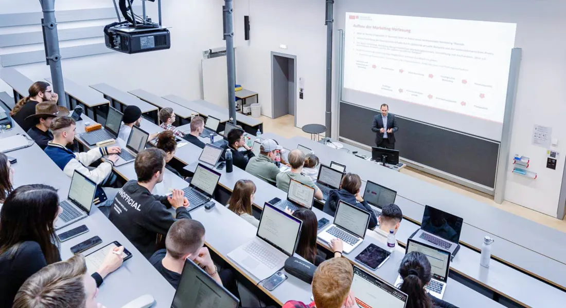 Professor erklärt Inhalte vor Studierenden mit Laptop und Notizen