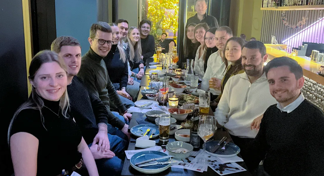 Große Gruppe junger Alumni sitzt beim Abendessen in einem Restaurant und tauscht sich über das Studium aus.