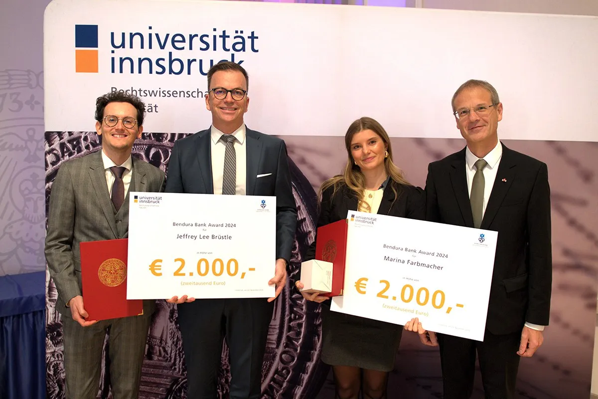 Vier Personen stehen nebeneinander und halten große Schecks mit der Aufschrift "Bendura Bank Award 2024" und einem Betrag von 2.000 Euro. Im Hintergrund ist ein Banner der Universität Innsbruck zu sehen. Die Personen sind formell gekleidet und lächeln in die Kamera.