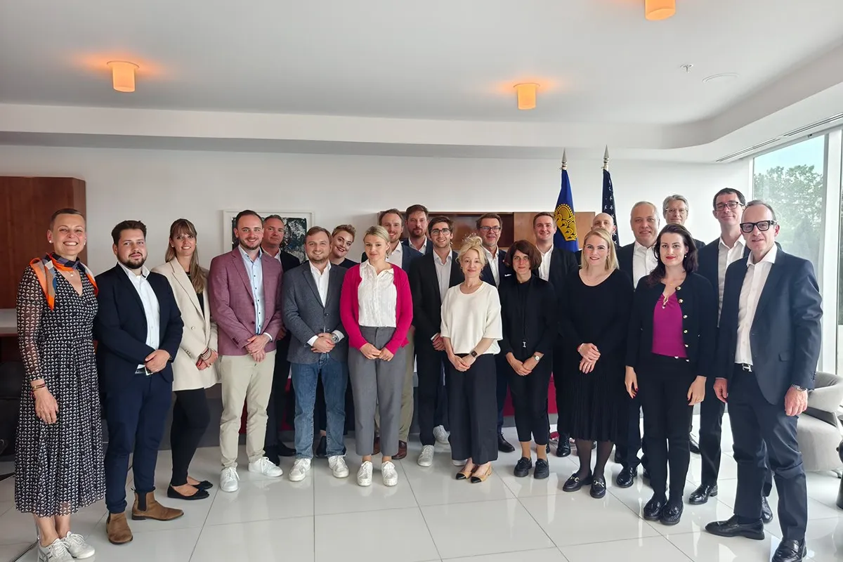 Gruppe von Studierenden und Dozenten des Executive Master of Laws (LL.M.) der Universität Liechtenstein während einer Studienreise in einem modernen Konferenzraum, im Hintergrund Flaggen.
