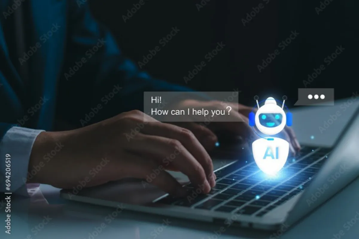 Ein Mensch tippt auf einer Laptop-Tastatur, während ein digitaler KI-Assistent auf dem Bildschirm erscheint und die Nachricht „Hi! How can I help you?“ anzeigt.