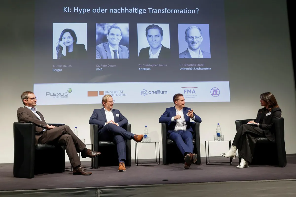 Eine Podiumsdiskussion an der Universität Liechtenstein über Künstliche Intelligenz mit vier Personen auf der Bühne. Im Hintergrund sind Porträts und Namen der Redner auf einer Leinwand zu sehen.