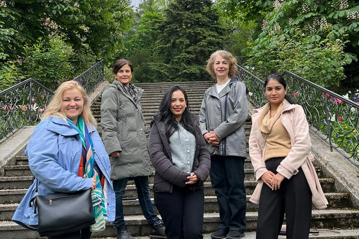 Fünf Personen stehen auf einer Treppe im Freien, umgeben von grünen Bäumen. Sie lächeln in die Kamera.