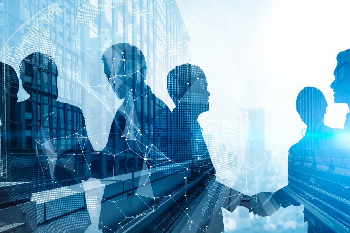 Silhouetten von Geschäftsleuten beim Handschlag mit vernetzter Weltkarte im Hintergrund.