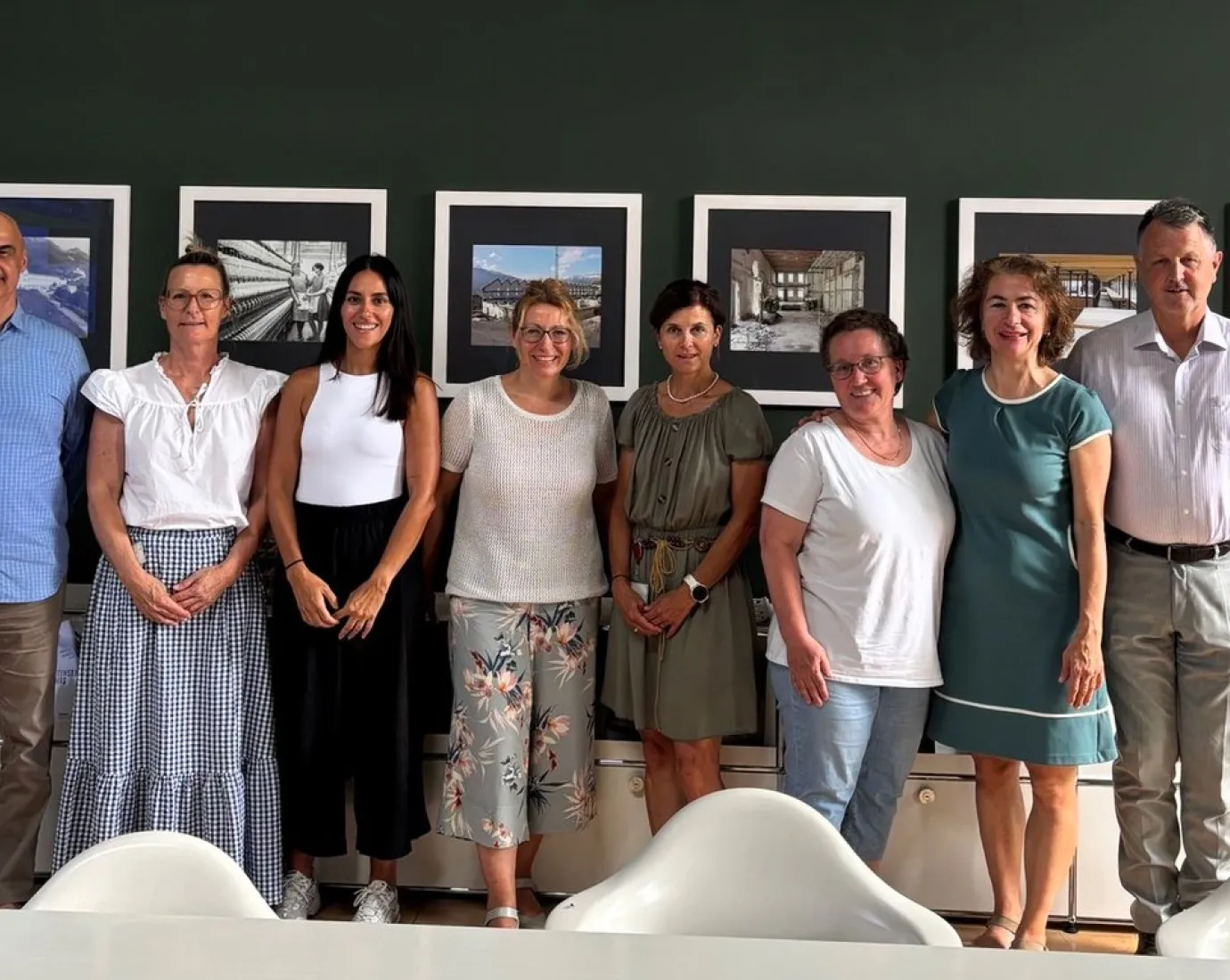 Eine Gruppe von acht Personen steht lächelnd vor einer Wand mit gerahmten Bildern. Sie befinden sich in einem Besprechungsraum der Universität Liechtenstein.