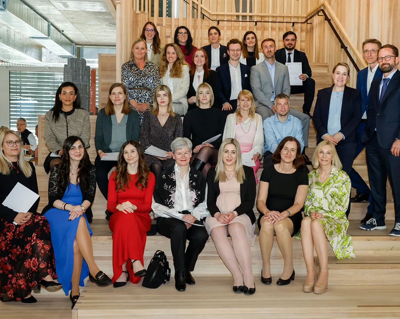 Gruppenfoto von Absolventinnen und Absolventen des Zertifikatsstudiengangs Treuhandwesen der Universität Liechtenstein, die auf einer Treppe sitzen und stehen. Sie halten Zertifikate in den Händen und lächeln in die Kamera. Im Hintergrund ist ein moderner Innenraum zu sehen.