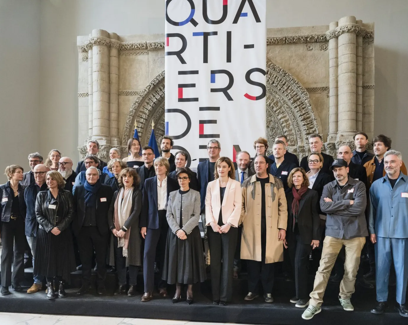 Gruppe von Architekten und Dozenten steht vor einem großen Banner mit der Aufschrift „Quartiers de demain“ in einem historischen Gebäude.