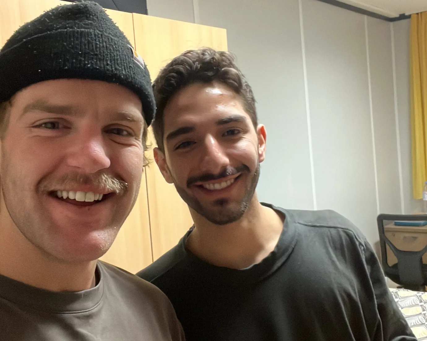 Two students smiling at the camera while holding beverage cans.