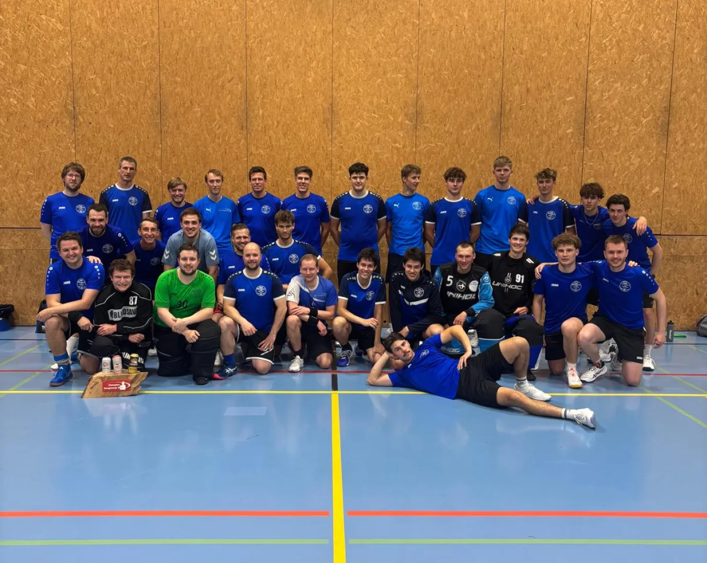 Group photo of a handball team wearing blue jerseys in a sports hall.