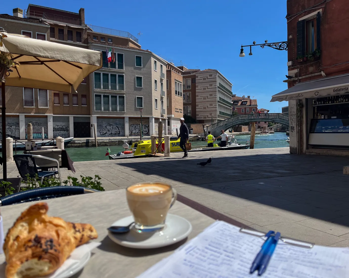 Coffee, croissant and notes on a table by a canal in Venice.