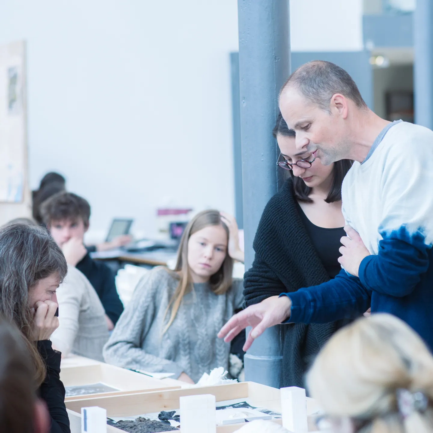 Dozent erklärt einer Studentin ein Architekturmodell, weitere Studierende verfolgen aufmerksam das Gespräch.