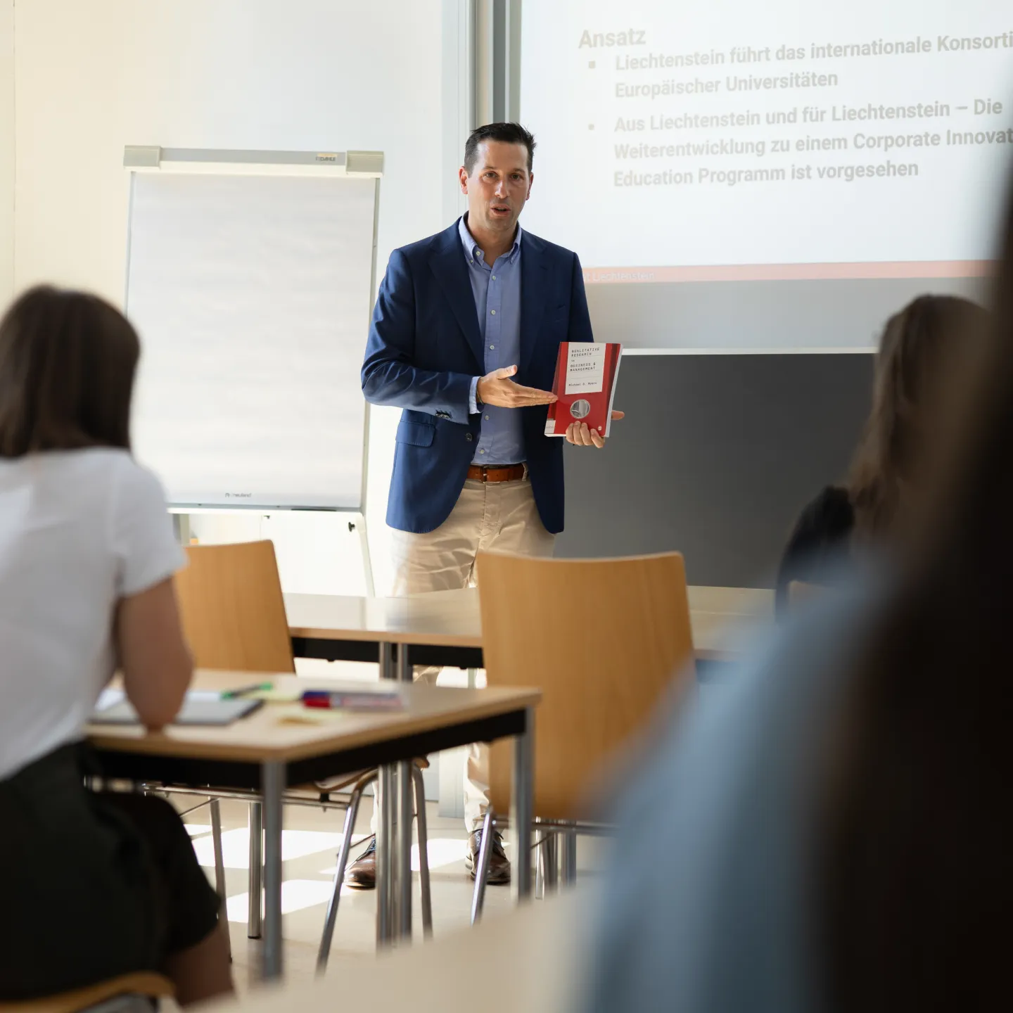 Dozent der Universität Liechtenstein präsentiert ein Fachbuch zum Thema Innovation vor Studierenden im Seminarraum.