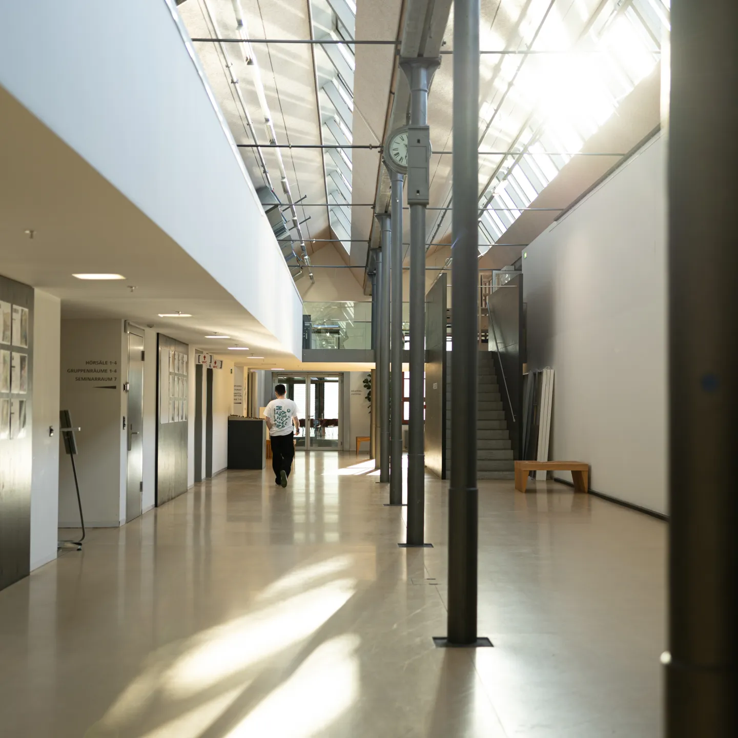Heller Flur mit Uhr, Sitzgelegenheiten und Zugang zu Hörsälen an der Universität Liechtenstein.