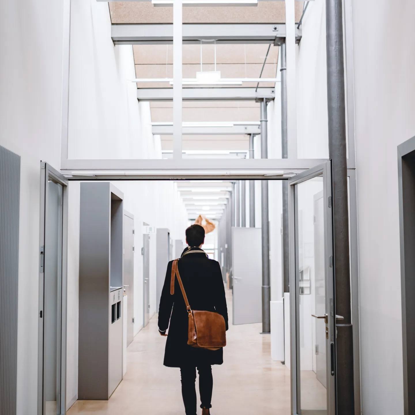 Studierende*r durchquert lichtdurchfluteten Hochschulflur der Universität Liechtenstein mit Dialektschrift an der Decke – modernes Campusambiente mit regionalem Bezug.