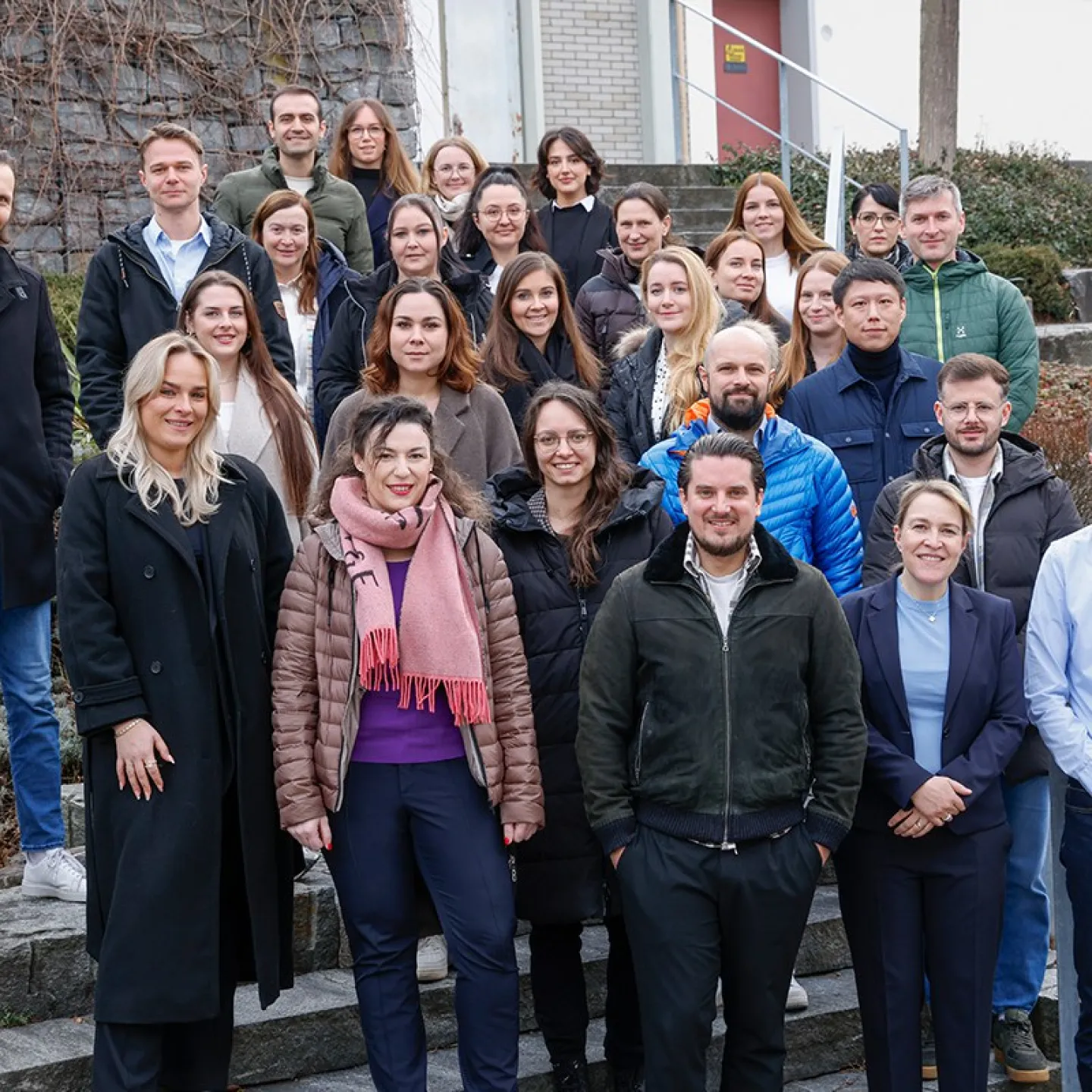 Gruppenfoto von Studierenden und Dozenten des Zertifikatsstudiengangs Compliance-Officer an der Universität Liechtenstein, aufgenommen auf einer Außentreppe. Die Gruppe lächelt in die Kamera, umgeben von winterlicher Vegetation.