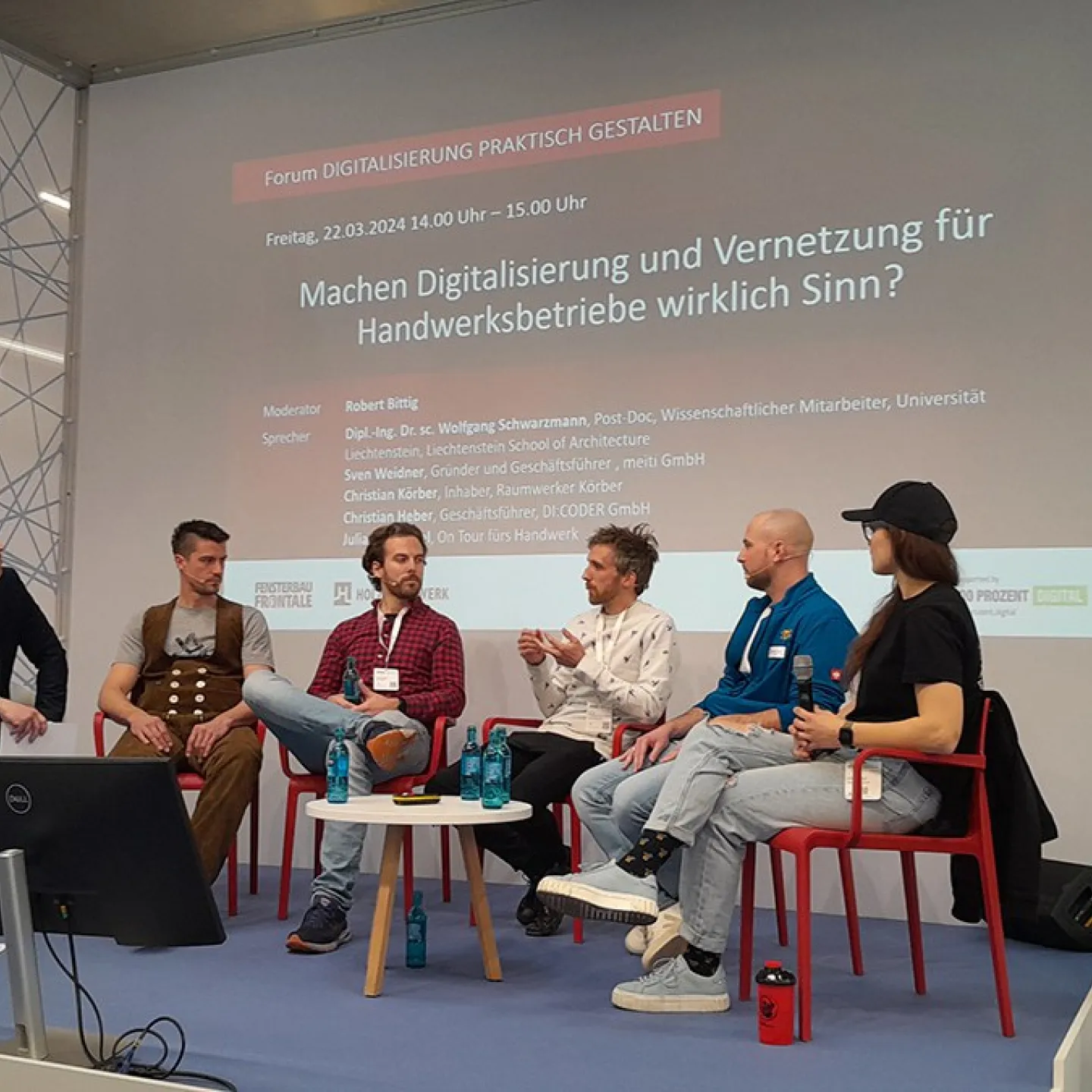 Podiumsdiskussion auf der Messe «Holz Handwerk 2024» in Nürnberg. Fünf Personen sitzen auf einer Bühne vor einer Leinwand mit dem Titel "Machen Digitalisierung und Vernetzung für Handwerksbetriebe wirklich Sinn?". Die Diskussion thematisiert die Rolle der Digitalisierung im Handwerk.