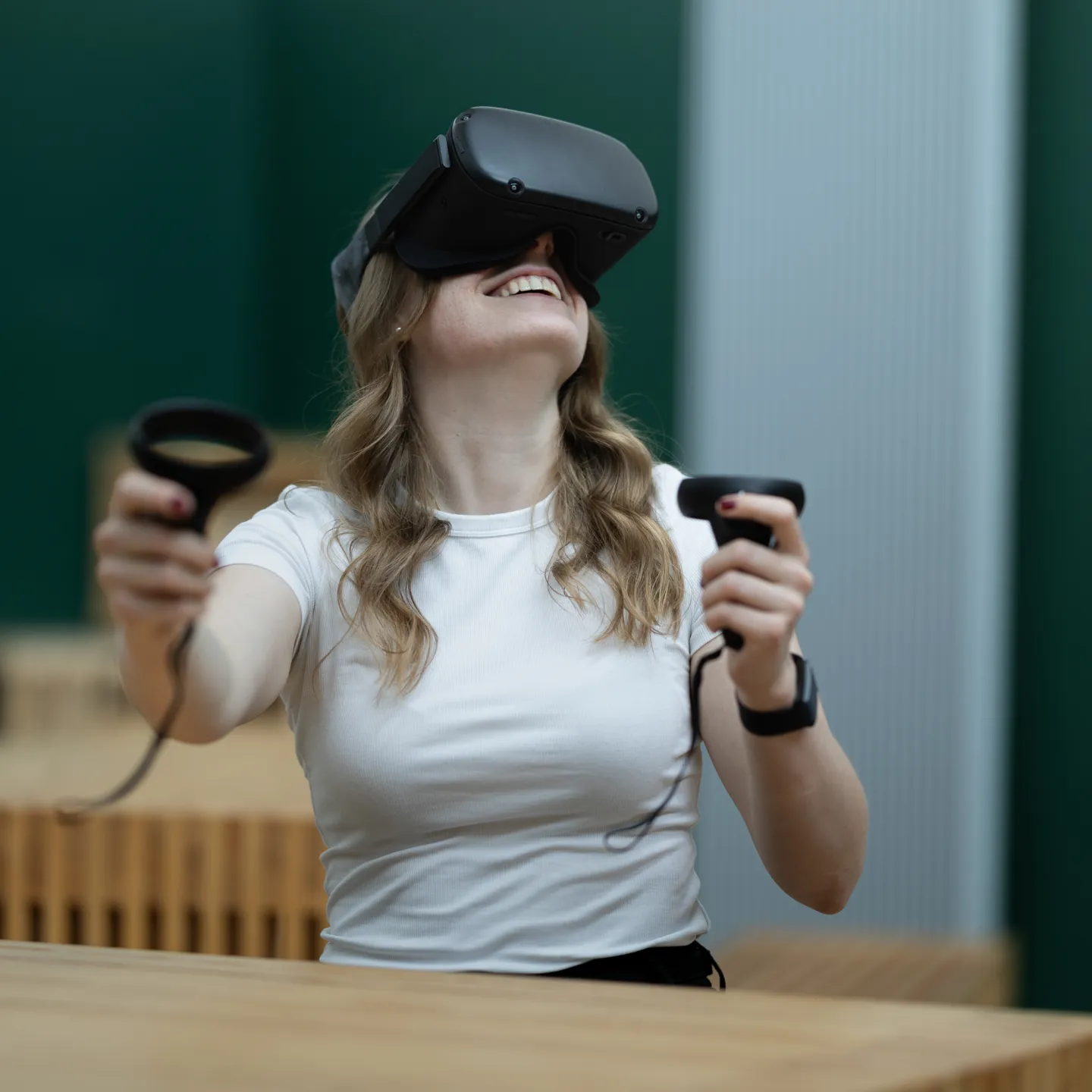 Studentin mit VR-Brille lacht und bewegt Controller im Klassenzimmer.