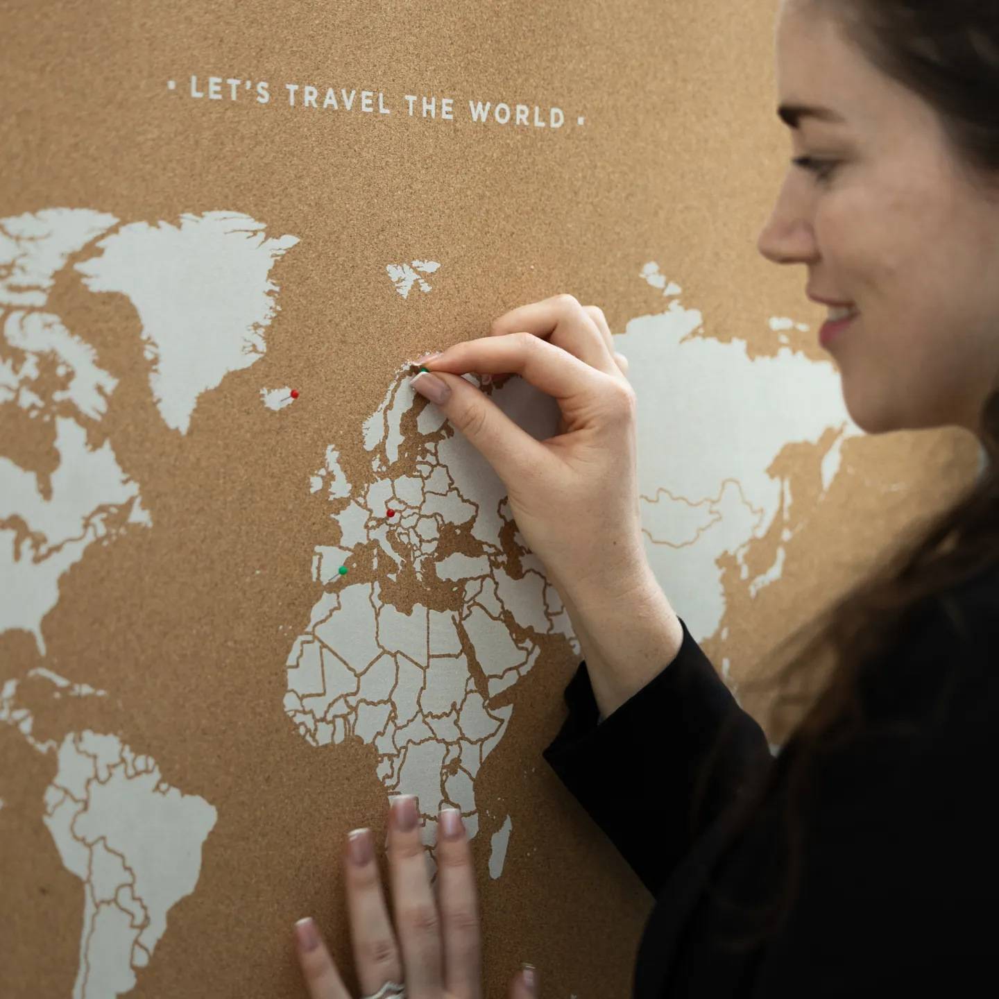 Frau steckt roten Pin in Weltkarte mit Aufschrift „Let’s Travel the World“.